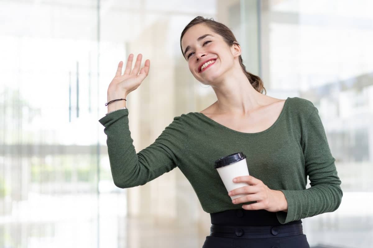 woman waving with coffee cup