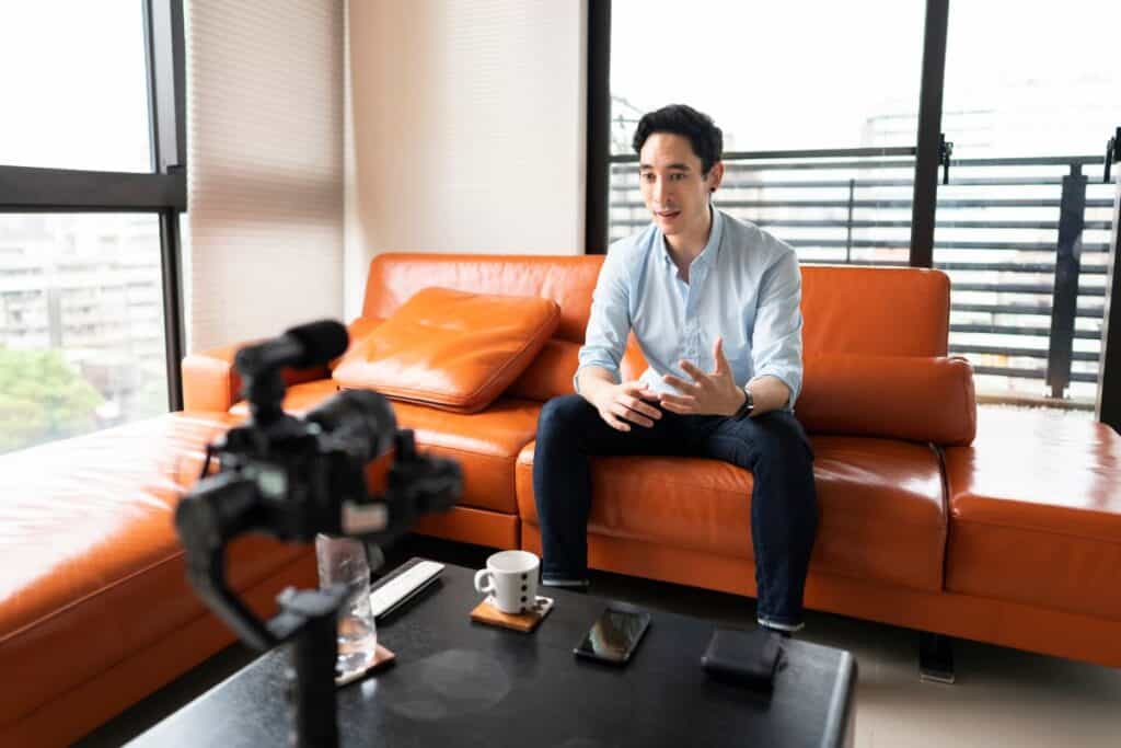 Man Filming Himself Taking To The Camera Sitting On An Orange Sofa